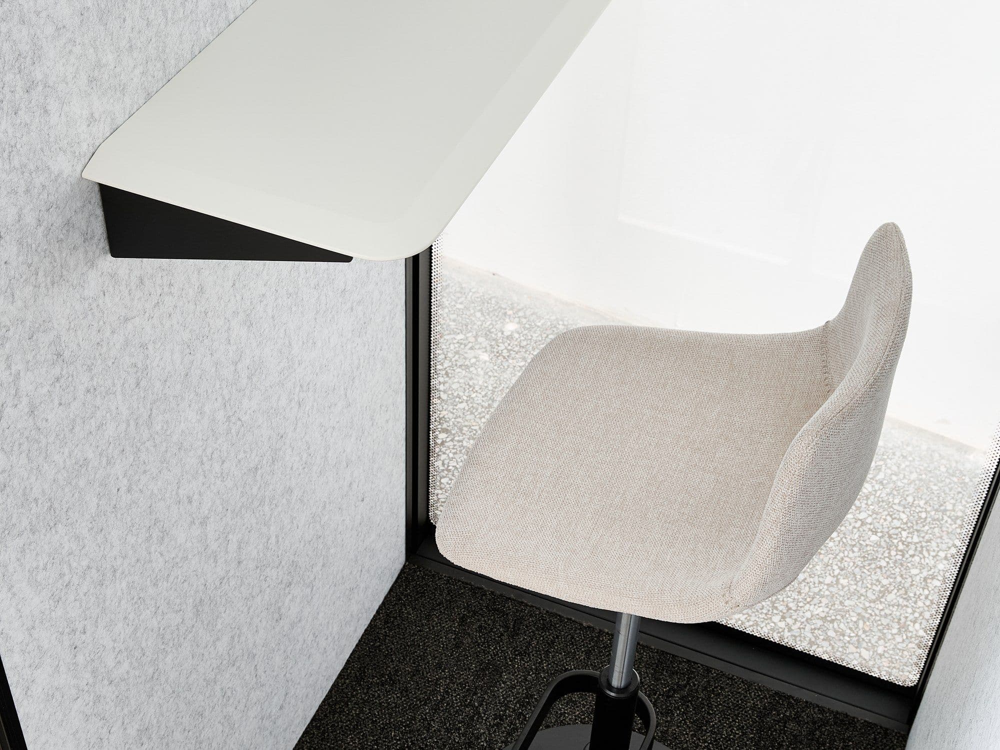 Inside an S-Pod, showing the white sit-stand desk and pale height-adjustable stool on the dark carpeted floor